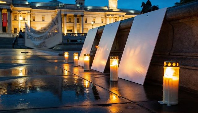 Evening vigil candles casting warm reflections on rain-slick urban square with blank placards