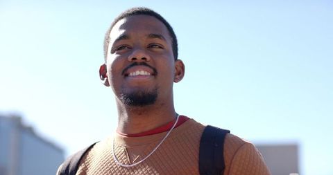 Young african american man smiling and looking up outdoors with backpack and casual sweater