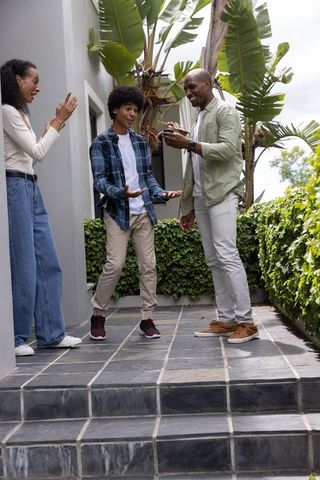 Multicultural family celebrating smartphone surprise on tropical porch with teenager