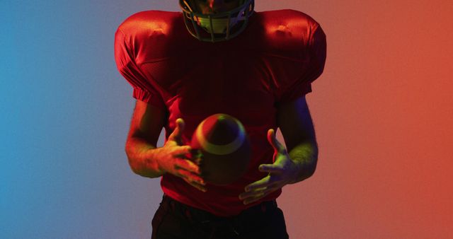 American football player in a red jersey and helmet practicing with ball under vibrant red and blue lighting. Ideal for content related to sports training, athletic determination, American football promotions, and dynamic sports visuals.