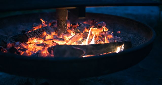 Captures vibrant glow of campfire embers in an outdoor fire pit during evening. Useful for camping, adventure, outdoors blogs, promotional materials for outdoor gear, and lifestyle magazines showcasing outdoor living.