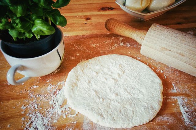 Fresh dough is on a wooden table next to a rolling pin and a basil plant. Ideal for use in blogs or articles about cooking, baking, or Italian cuisine. Great for cooking classes, recipe books, or kitchen decor inspiration.