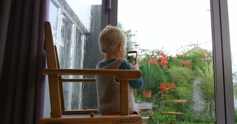 Young boy using smartphone to capture rainy view indoors