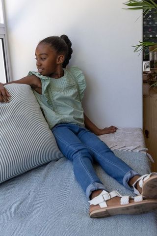 African american girl relaxing on sunlit window seat leaning against striped pillow
