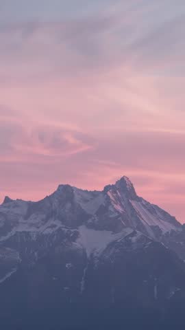 Vertical sunrise bathing snowcapped alpine peak in pastel light with drifting clouds