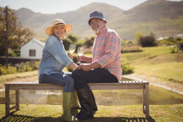 Senior couple sitting on a bench in a scenic outdoor setting, enjoying white wine together. Ideal for use in advertisements for retirement communities, lifestyle blogs, travel brochures, or health and wellness articles focusing on active aging and enjoying life.