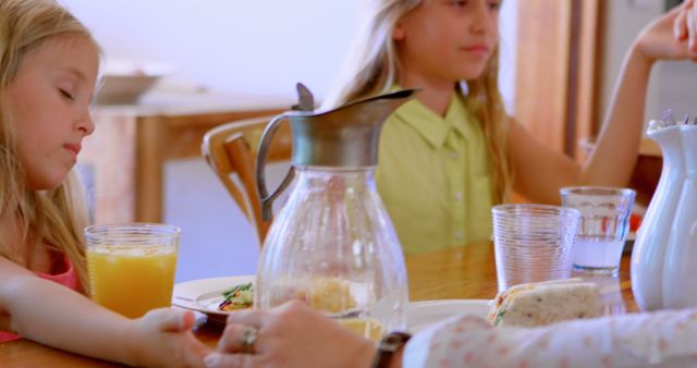 Children enjoy breakfast together at the table with orange juice and sandwiches. Ideal for family, children, or morning lifestyle images. Perfect for illustrating warmth, togetherness, and daily routines in family promotional materials.