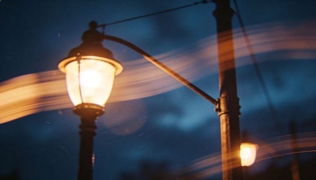 Vintage street lamp glowing at dusk with warm light trails and moody blue hour
