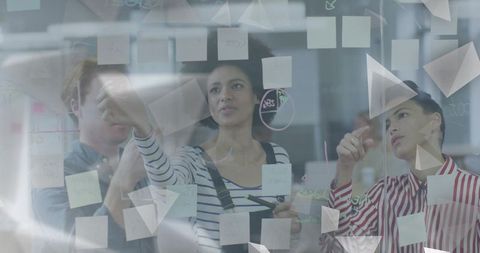 Collaborative team brainstorming on glass wall with sticky notes and strategy diagrams