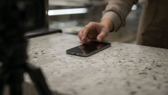 Barista reaching for smartphone on speckled terrazzo counter with tripod leg in cafe