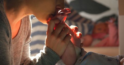 Mother Lovingly Kissing Baby's Feet in Warm Sunlight