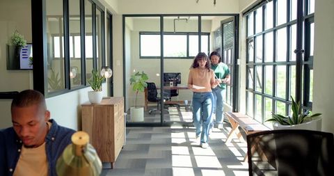 Diverse team walking through bright modern glass office corridor holding papers and tablet