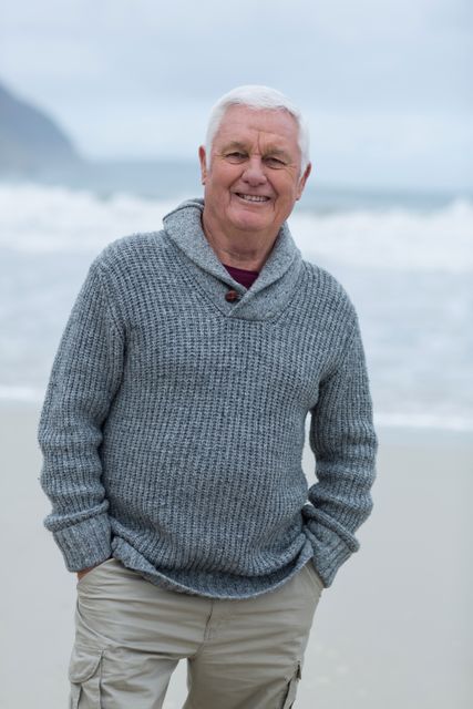 Senior man standing on a beach, smiling while enjoying the ocean view. Great for use in travel advertisements, health and wellness campaigns, retirement planning brochures, and lifestyle blogs focusing on seniors.