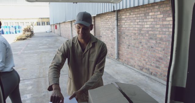 Young African American man working in a delivery area, with copy space. He is unloading cardboard boxes from a vehicle at an outdoor loading dock.