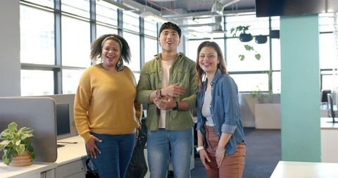 Smiling diverse coworkers posing in bright open-plan office with plants and teamwork energy