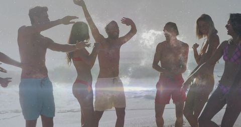 Backlit sunlit beach party with friends laughing and celebrating on shoreline in swimwear