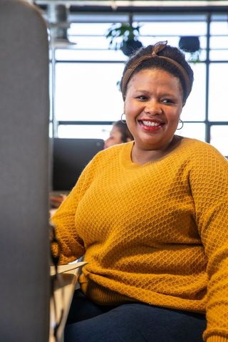 Smiling African American Woman Wearing Mustard Sweater at Modern Open-Plan Office Desk