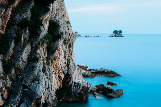 Capturing the serene beauty of a coastal cliff with rugged rock formations against the backdrop of a calm, blue sea. Ideal for travel guides, nature magazines, wallpaper backgrounds, and websites promoting coastal tourism and adventure.