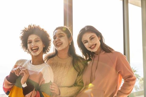 Diverse friends enjoying facial masks and cozy knitwear during sunlit self-care moment