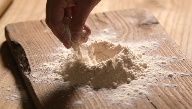 Hand sprinkling flour into well on rustic wooden board for homemade bread, pastry baking