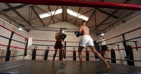 Boxer landing powerful hook in ring while opponent retreating and trainer observing