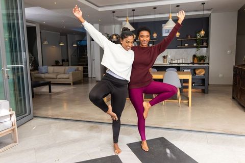 Indian and african american women practicing paired yoga balance in modern open-plan home