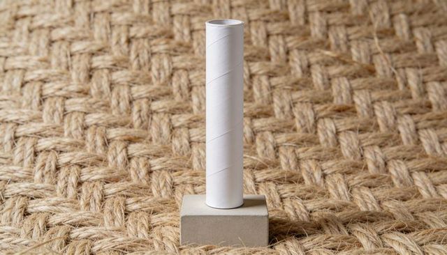 Minimal white paper roll core standing on concrete block over woven jute mat
