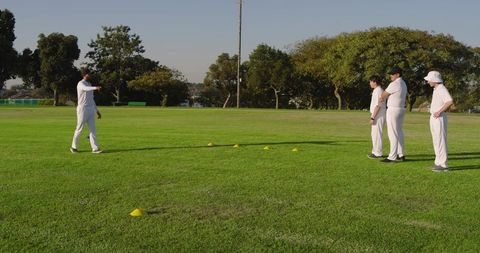 Cricket coaching session with players practicing field drills on sunlit grassy ground