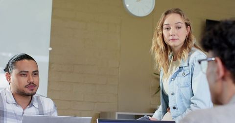 Young professionals collaborating at table, woman wearing denim jacket leading meeting