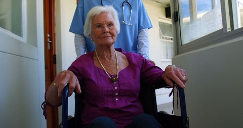 Doctor in nursing home assisting senior woman in wheelchair