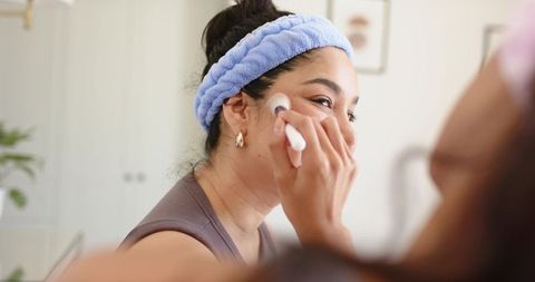 African american woman applying blush at home vanity, practicing skincare and self care