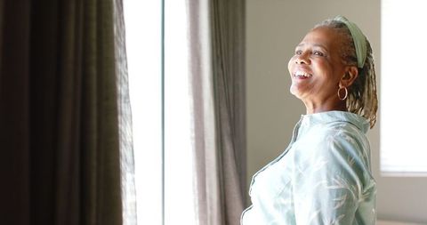 African American Senior Woman Opening Curtains in Warm Light