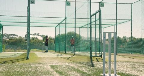 Practicing cricket in outdoor nets with multicultural players, batting and bowling action