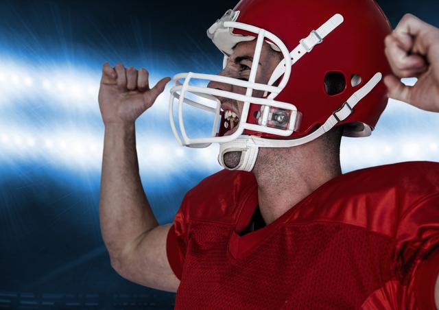 Football player in red jersey and helmet celebrating victory under bright stadium lights. Ideal for use in sports promotions, motivational posters, team spirit campaigns, and advertisements related to football or athletic achievements.