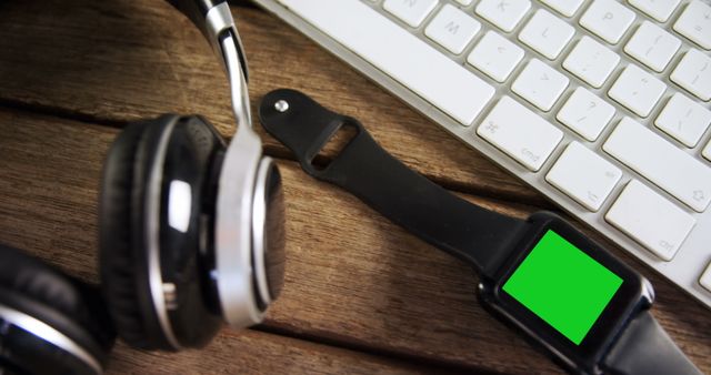 Headphones, smartwatch, and keyboard placed on a wooden table highlighting tools for a modern and productive workspace. Ideal for use in articles and advertisements about technology, home office setups, or productivity tools.