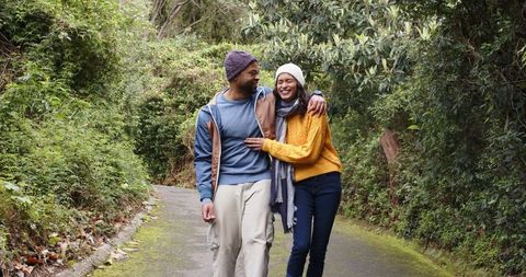 Walking together on mossy forest path, diverse couple enjoying autumn walk and laughter