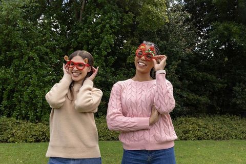 Mixed-ethnicity friends wearing festive red novelty glasses in garden smiling and laughing