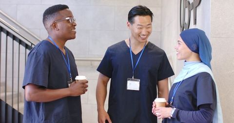Diverse healthcare team chatting and smiling during coffee break in hospital corridor