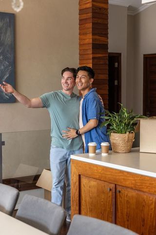 Diverse male friends unpacking at modern kitchen island, celebrating new home move