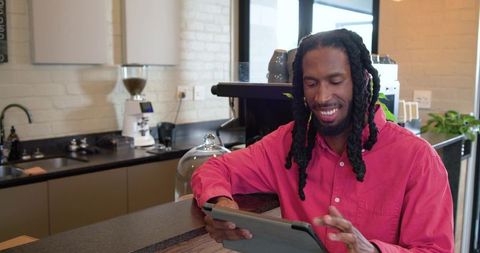 African american man using tablet at cafe counter wearing pink shirt and smiling