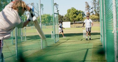 Diverse men practicing cricket in outdoor net enclosure during fast-paced training session