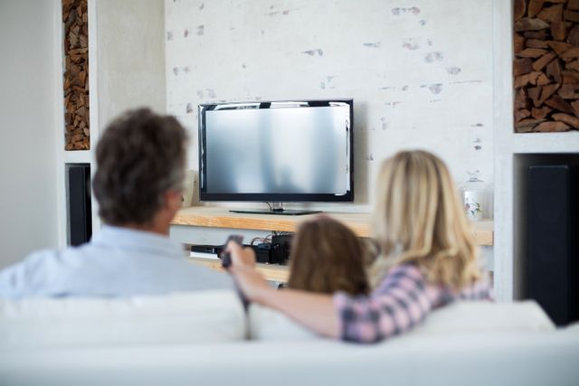 Rear view of family watching television in living room at home