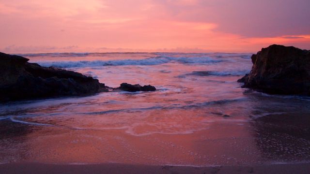 Peaceful evening over a rocky beach with calming ocean waves and a stunning pink sky. Ideal for travel websites, nature blogs, backgrounds, or inspirational posters highlighting tranquility and natural beauty.