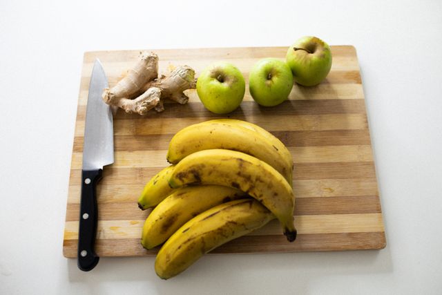 Fruits and ginger with carving knife on wooden chopping board. healthy raw foods eating lifestyle at home, apples, bananas.