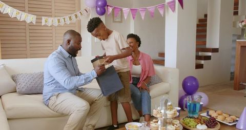 African american family celebrating birthday at home son giving gift to father party decorations