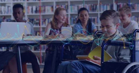 Inclusive classroom student in wheelchair reading while classmates collaborate on laptops