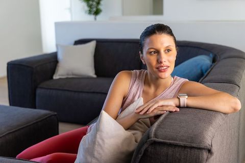 African american woman relaxing on gray sectional sofa wearing smartwatch in modern living room