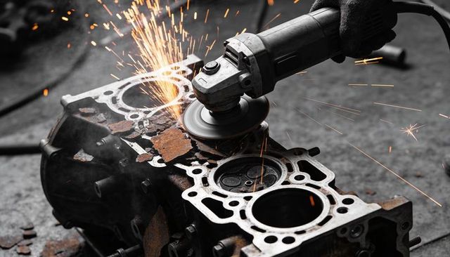 Angle grinder grinding rusted engine block with flying sparks in mechanic workshop