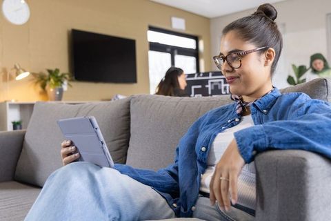 Young woman sitting on sofa using tablet in modern coworking lounge with diverse team
