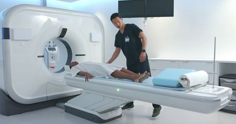 African american woman undergoing ct scan while asian radiology technologist adjusting patient